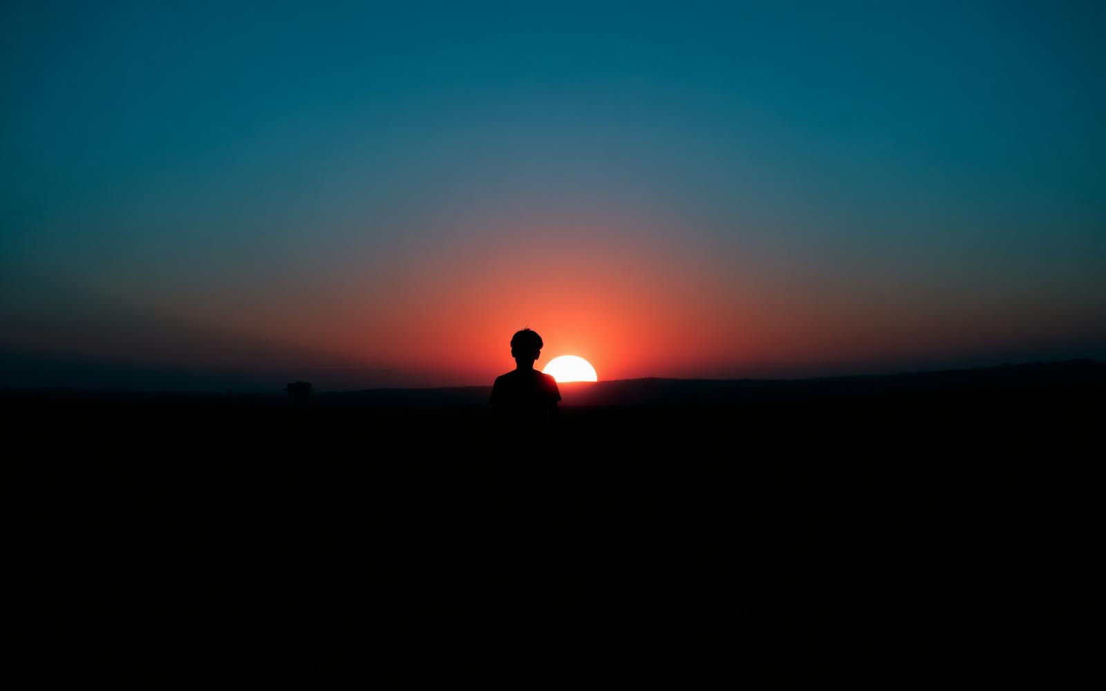 A person walking along a softly lit path toward a distant horizon.